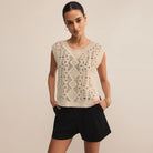 Woman wearing a beige lace top and black shorts against a beige background