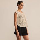 Woman wearing a beige lace top and black shorts against a beige background