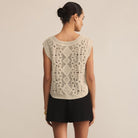 Woman wearing a beige sleeveless knitted top with a textured pattern on a plain background
