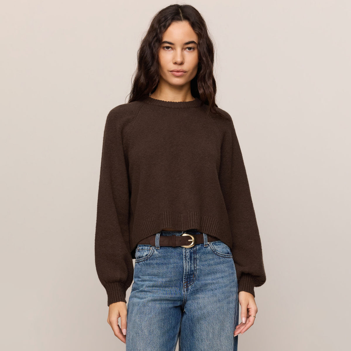 Woman wearing a brown sweater and blue jeans against a beige background