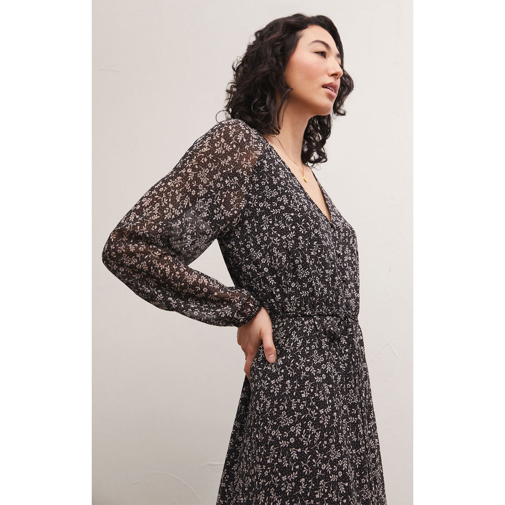 Brunette model wearing Z Supply Della Floral Midi Dress in Black with black boots in front of a white background