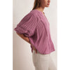 Side view of Model wearing Z Supply Elliot Lace Inset Top in Dusty Orchid with white jeans