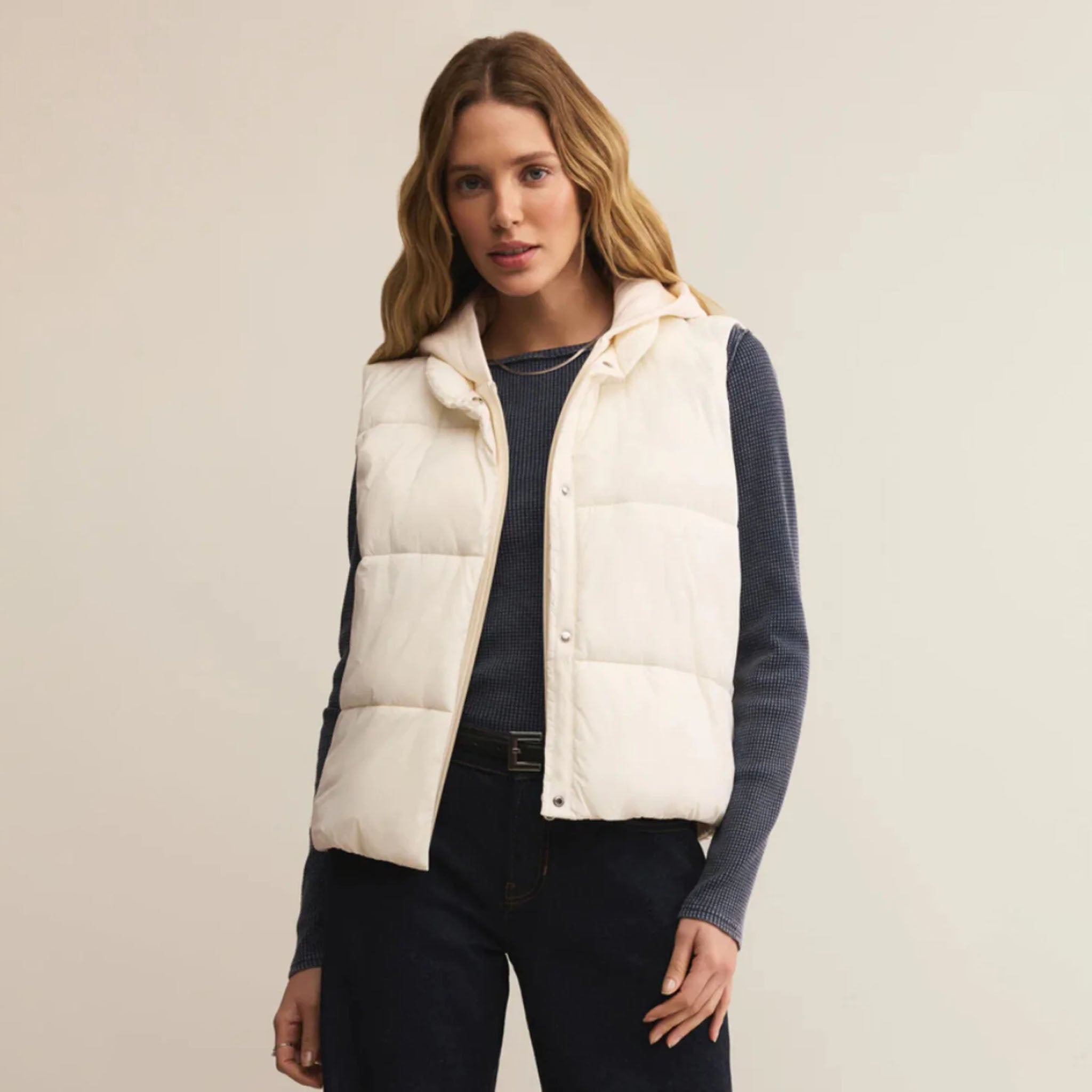 Woman wearing a white puffer vest over a dark outfit on a plain background