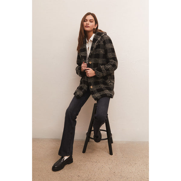 Model wearing black pants and loafers and Z Supply Hastings Sherpa Coat In Black sitting on a black stool in front of a neutral wall