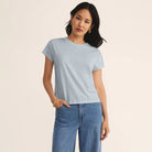Woman wearing a light blue t-shirt, the Z Supply Modern Slub Tee in Clearwater, and jeans on a beige background