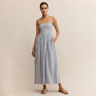 Woman wearing Z Supply Nadine Striped Midi Dress in Boathouse which is a blue and white striped dress on a beige background