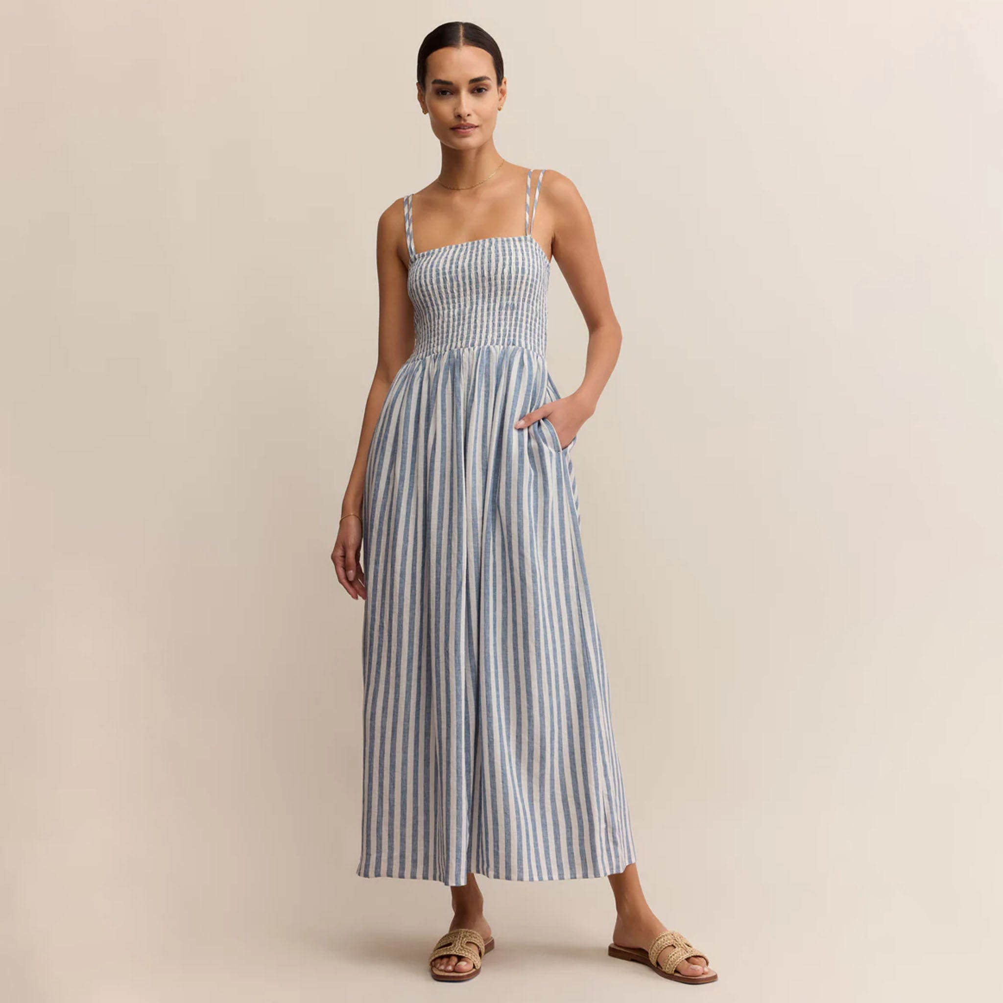 Woman wearing Z Supply Nadine Striped Midi Dress in Boathouse which is a blue and white striped dress on a beige background