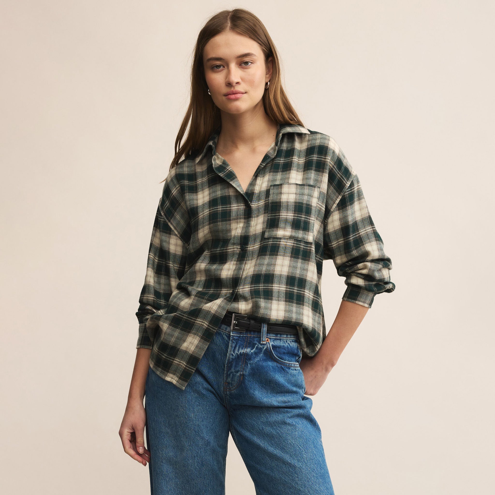 Woman wearing a plaid shirt and jeans against a beige background