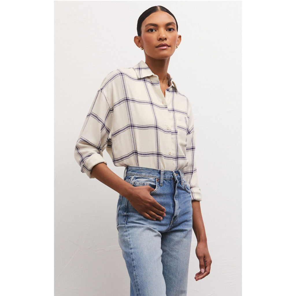 Model wearing jeans and Z Supply River Plaid Button Up in Inca in front of a white wall