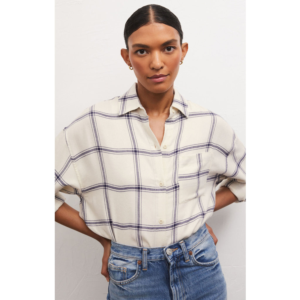 Model wearing jeans and Z Supply River Plaid Button Up in Inca in front of a white wall