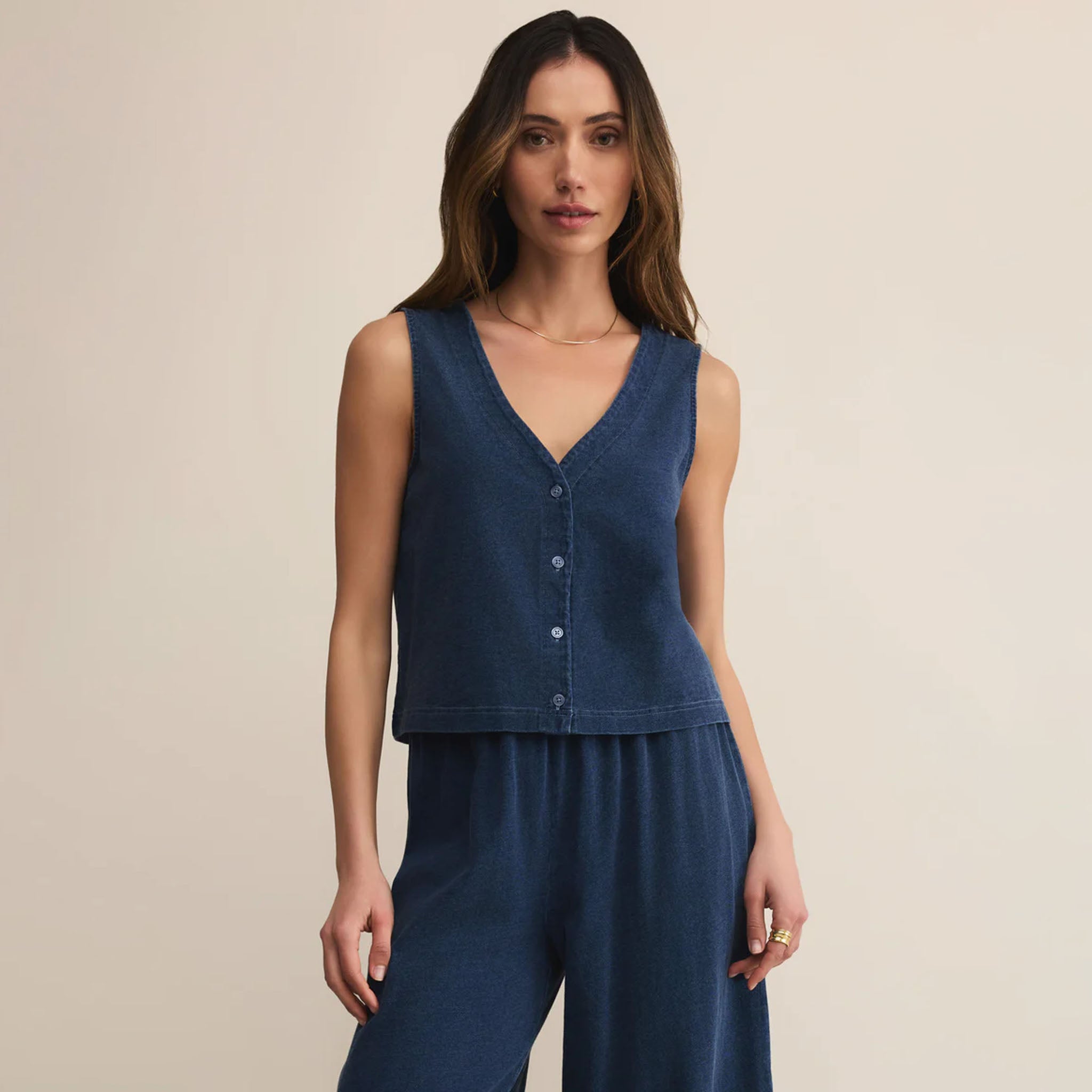 Woman wearing a blue sleeveless top and pants on a beige background