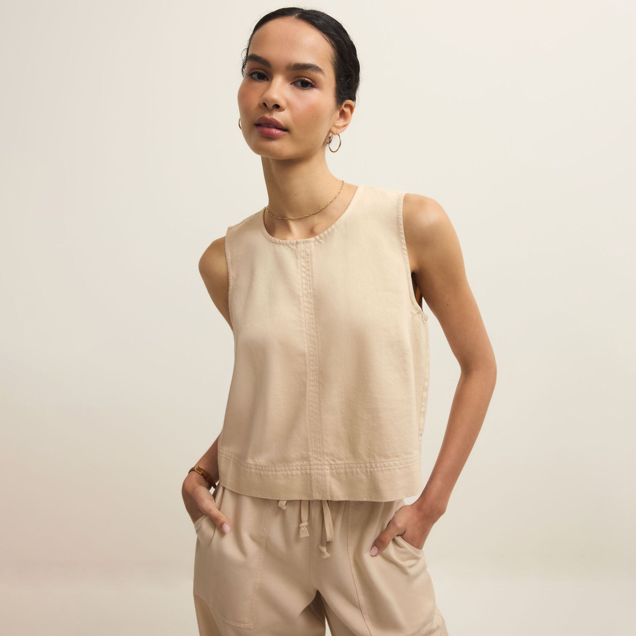 Woman wearing a beige sleeveless top and pants against a plain background