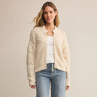 Woman wearing Z Supply Sundance Sweater Jacket in Crystal, a beige cardigan over a white shirt and blue jeans on a plain background