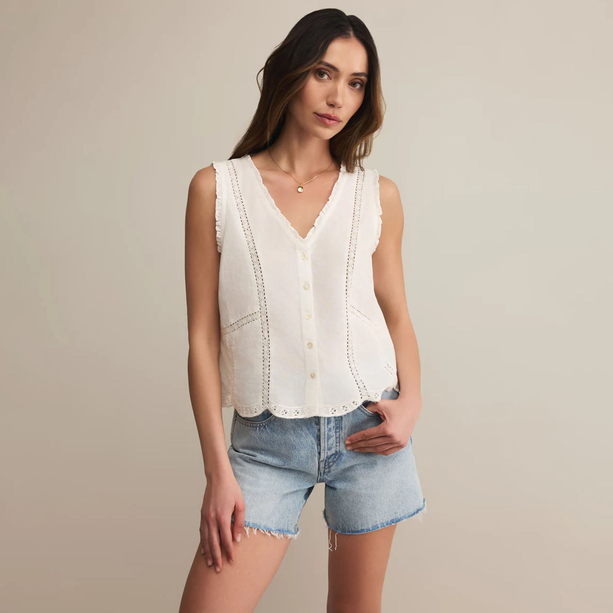 Woman wearing a white sleeveless top and denim shorts against a beige background