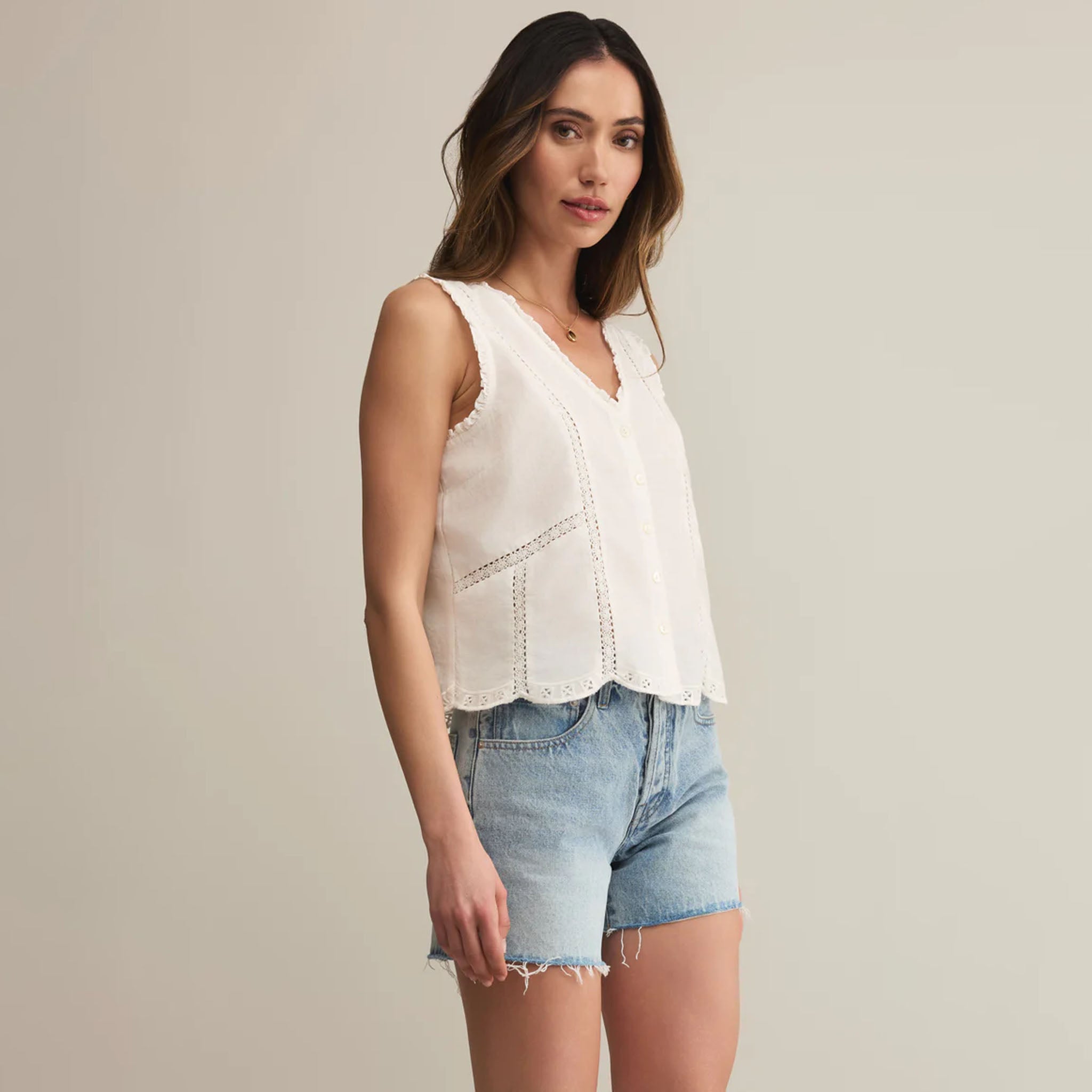 Woman wearing a white sleeveless top and denim shorts on a plain background