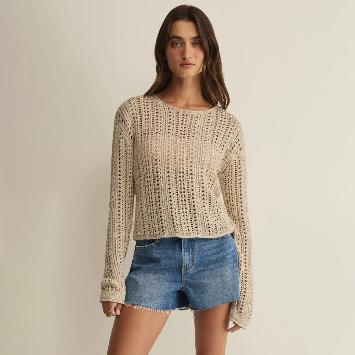 Woman wearing a beige knitted sweater and denim shorts on a plain background