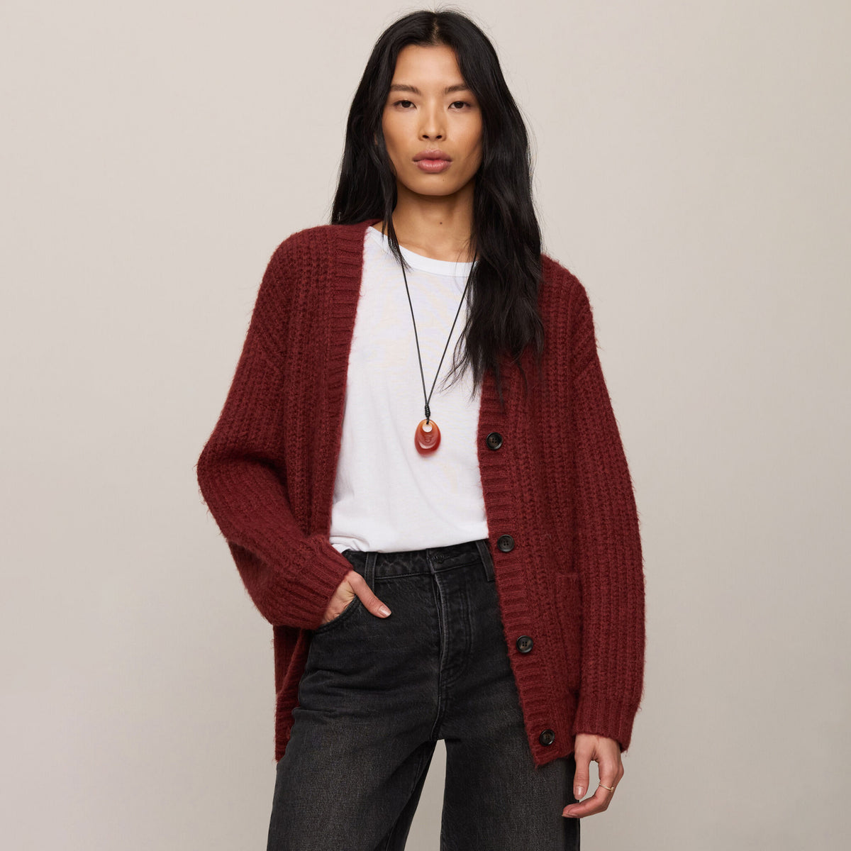 Woman wearing a red cardigan over a white shirt and dark jeans on a beige background