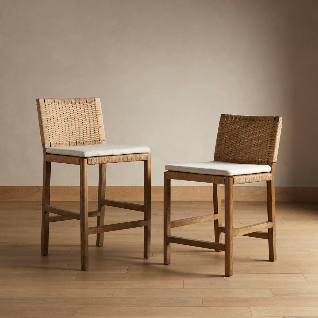 Four Hands Zuma bar stool and counter stool with beige cushion and woven back in Dune Ash on a wood floor in front of a beige wall