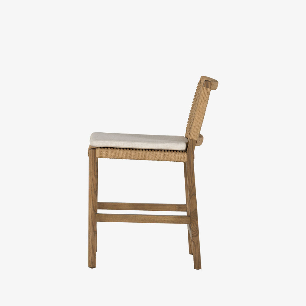Four Hands Zuma counter stool with beige cushion and woven back in Dune Ash on a white background
