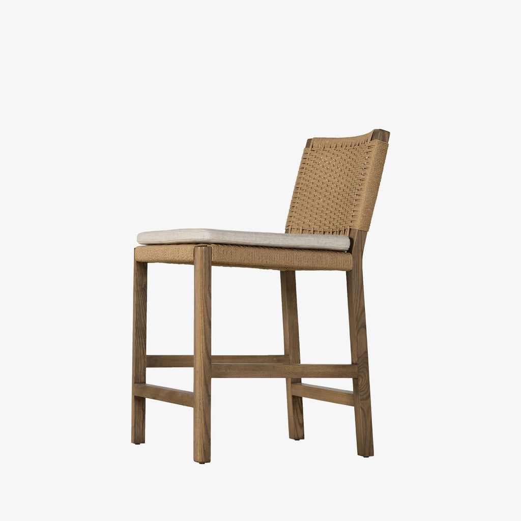 Four Hands Zuma counter stool with beige cushion and woven back in Dune Ash on a white background