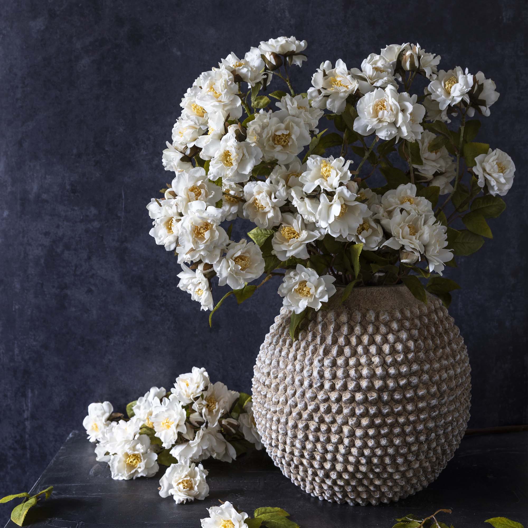 Abigail Ahern Artificial Rose Sprays in Cream in a light colored pot with texture on a black background