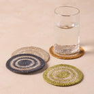 Set of four crocheted coasters with a glass of water on a beige surface
