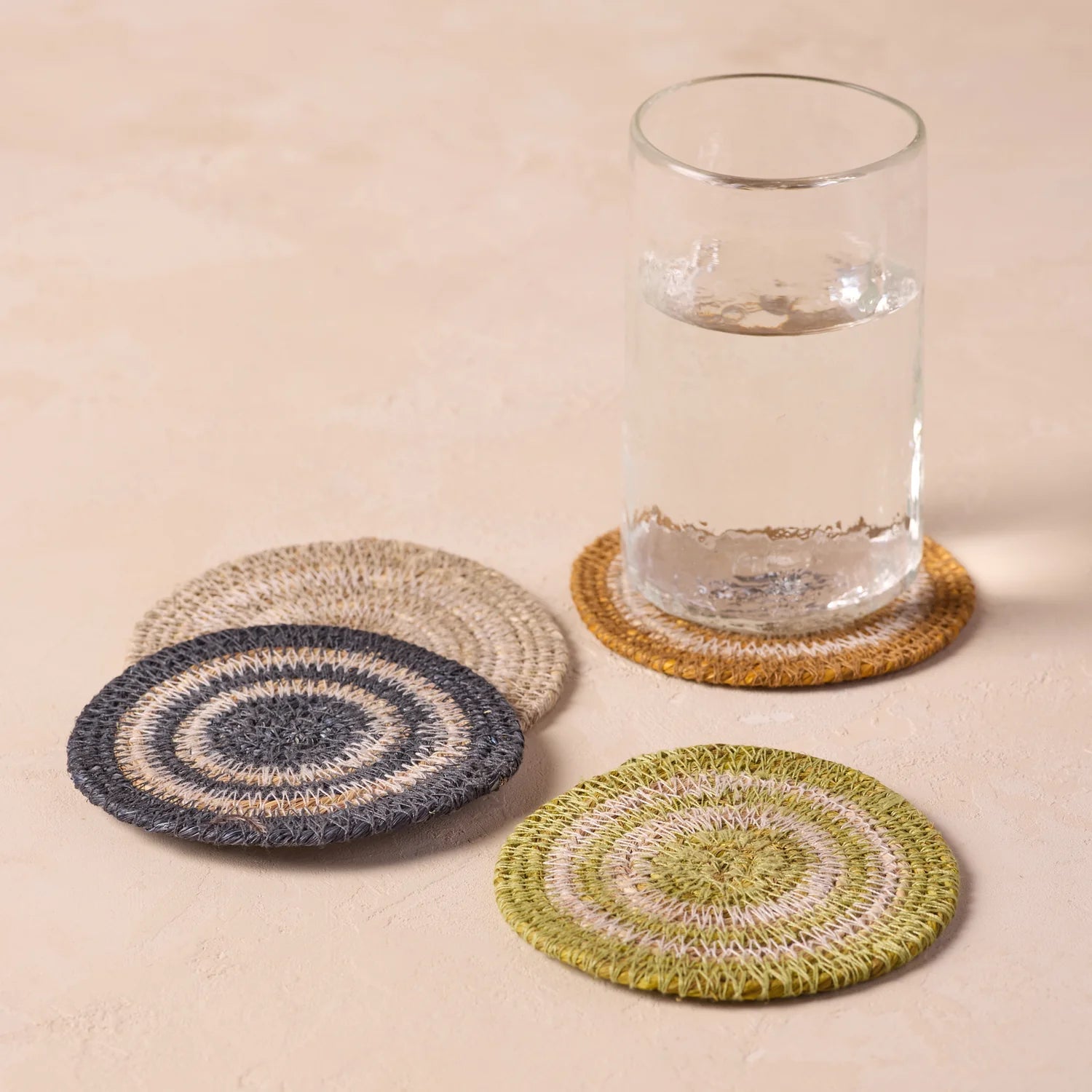 Set of four crocheted coasters with a glass of water on a beige surface