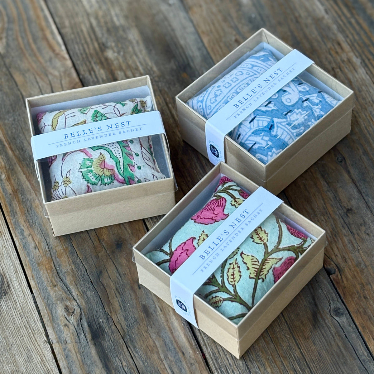 Three small lavender sachet boxes with floral designs on a wooden surface