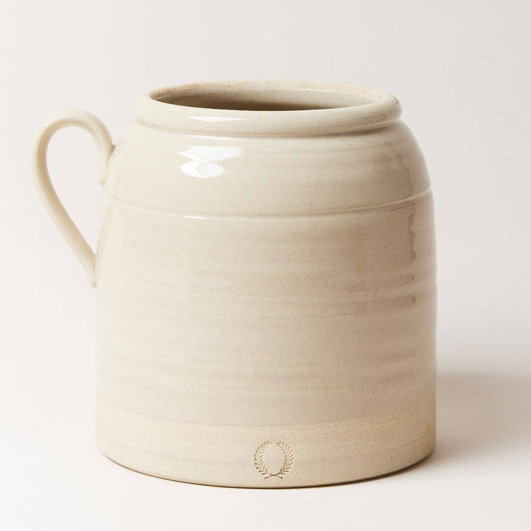 Beige ceramic crock with a handle on a white background
