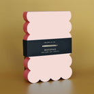 Pink and red scalloped notepad with a black label on a gold background