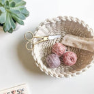 Woven basket with yarn balls and scissors on a light surface, next to a succulent plant.