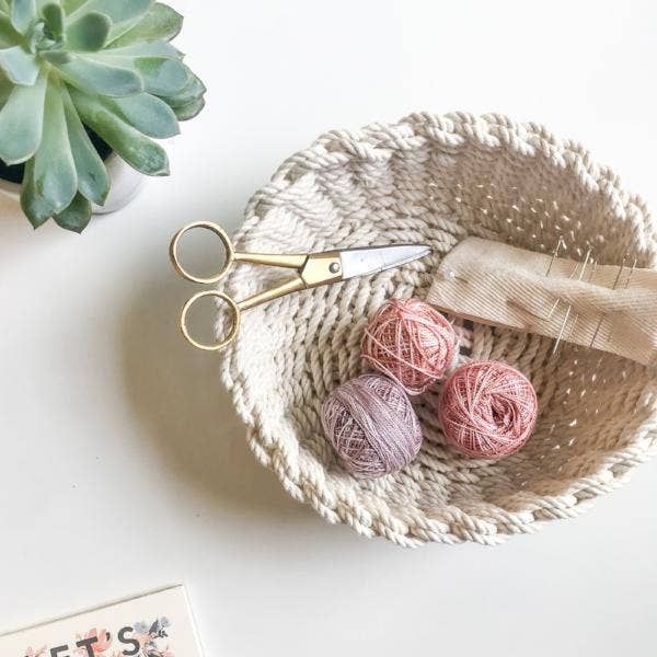 Woven basket with yarn balls and scissors on a light surface, next to a succulent plant.