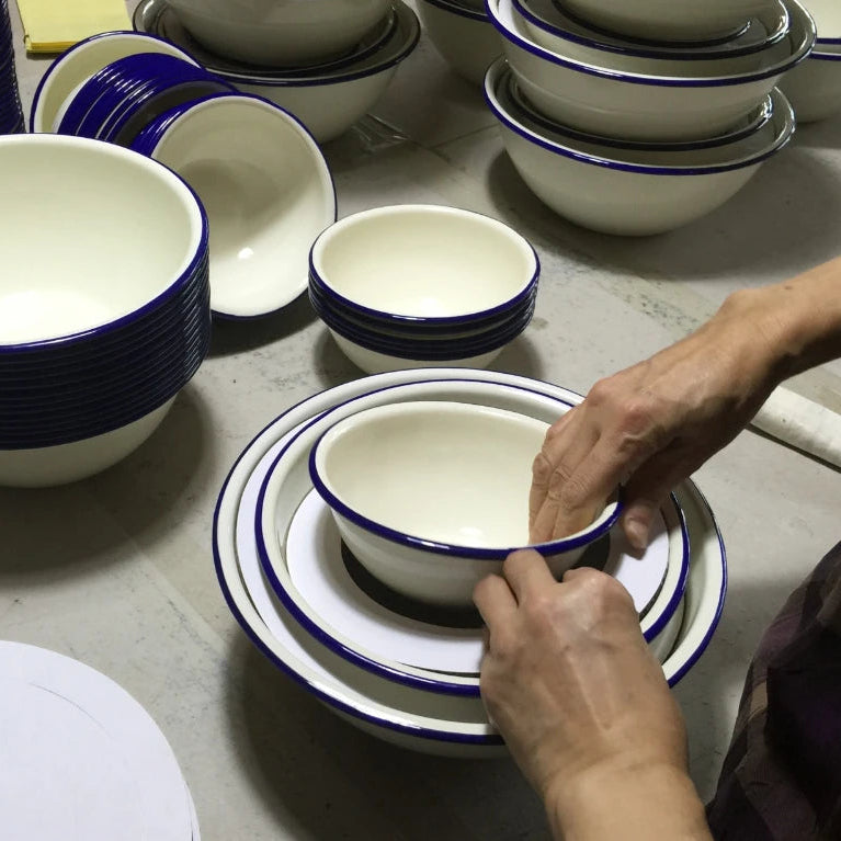 Person arranging enamelware bowls with blue rims on a table.