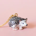 Camp hollow porcelain necklace with porcupine figurine on a chain against a light pink background.