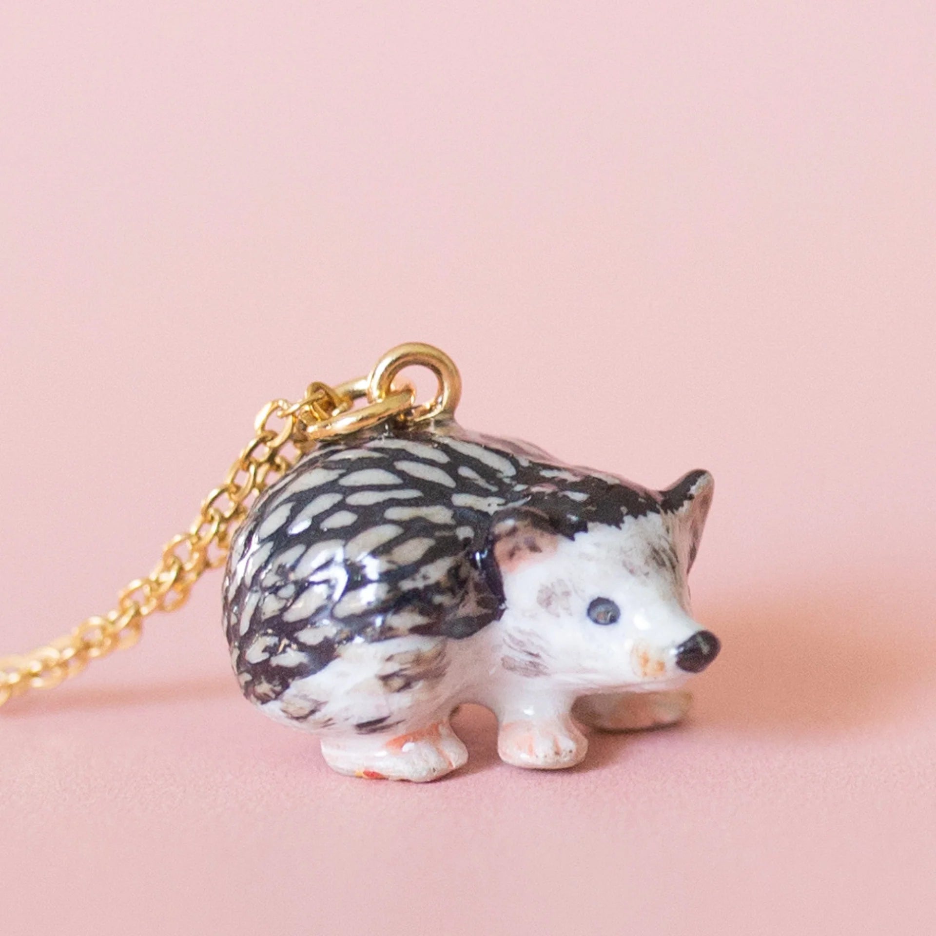 Camp hollow porcelain necklace with porcupine figurine on a chain against a light pink background.