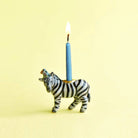Zebra-shaped candle holder with a lit blue candle on a yellow background