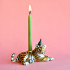 Candle holder shaped like a tiger with a lit green candle on a pink background