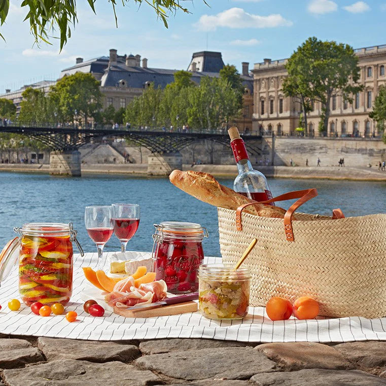 Picnic setup by a river with wine, food, and a basket in Paris.
