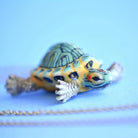 Camp hollow porcelain necklace with turtle figurine on a chain against a light blue background.