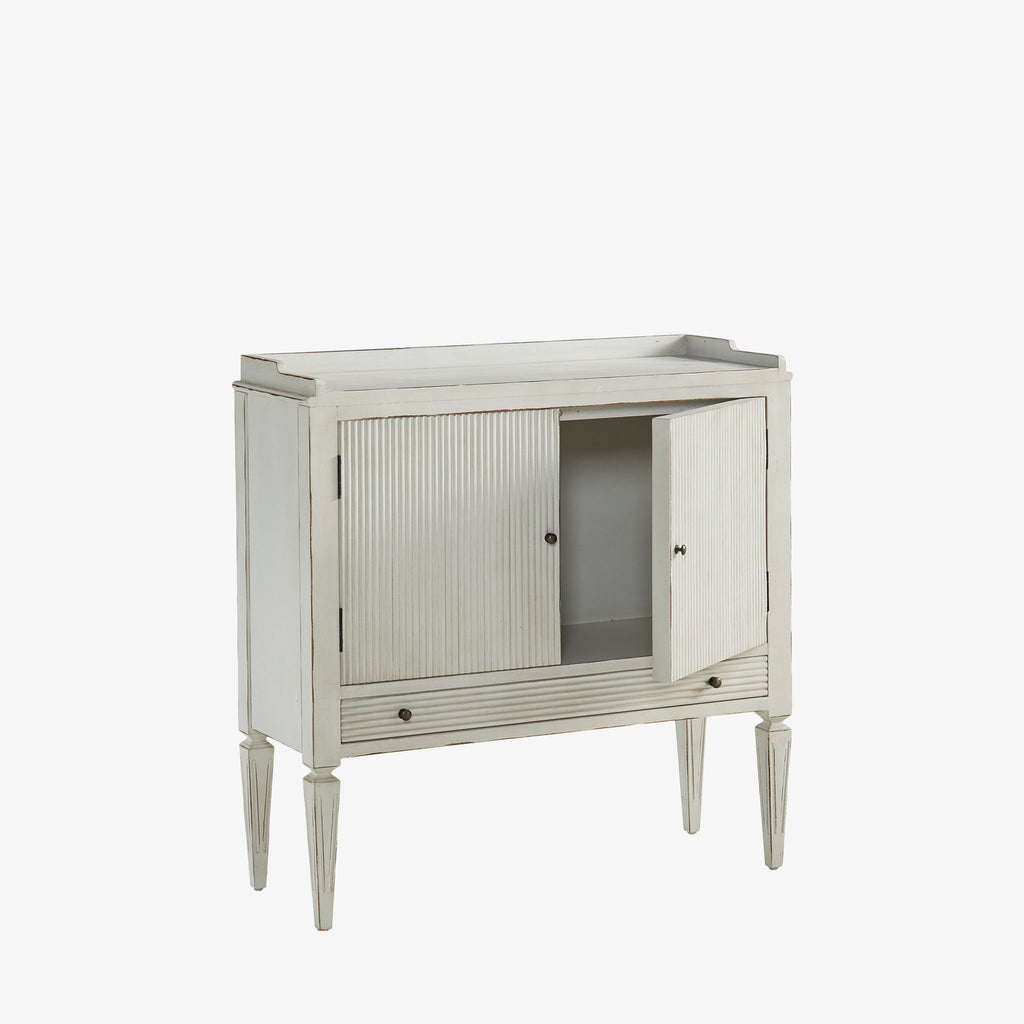 Whitewashed small console cabinet with reeded doors and tapered feet on a white background
