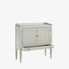 Whitewashed small console cabinet with reeded doors and tapered feet on a white background