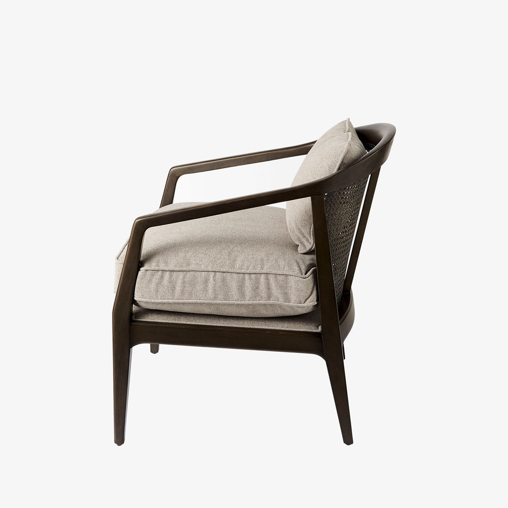 Armchair with dark brown stain and sloped arms and cane back and light beige cushions on a white background