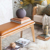 Wood bench with leather seat cushion in living room space with books and accessories