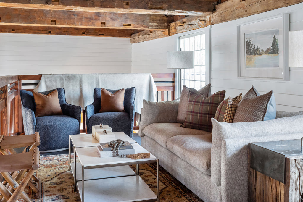 Sitting area with cream sofa, grey arm chairs, wood beams and two folding leather and wood stools. 