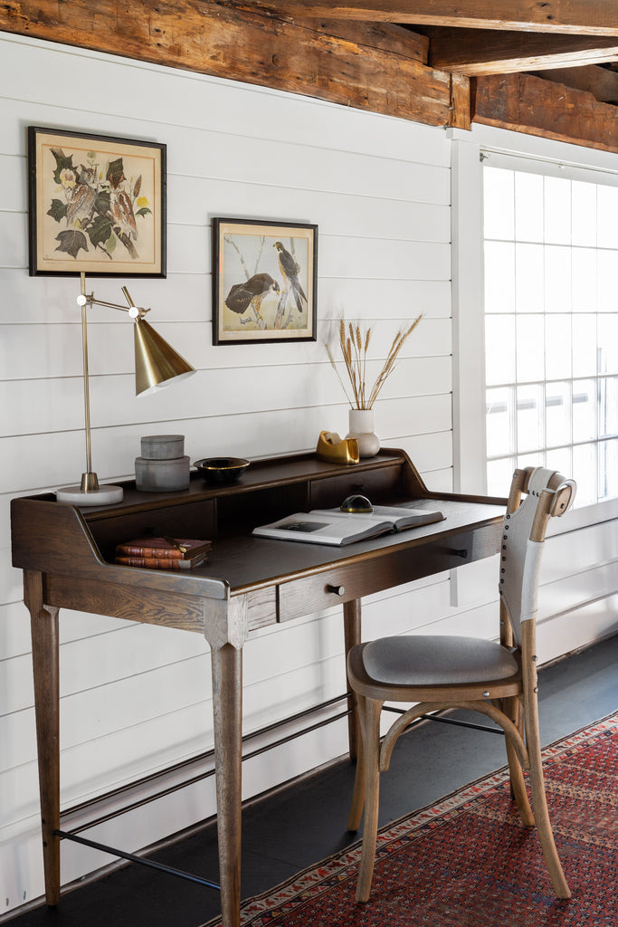 Wood desk in room with beams and shiplap siding and bistro chair with wrapped canvas on red antique rug