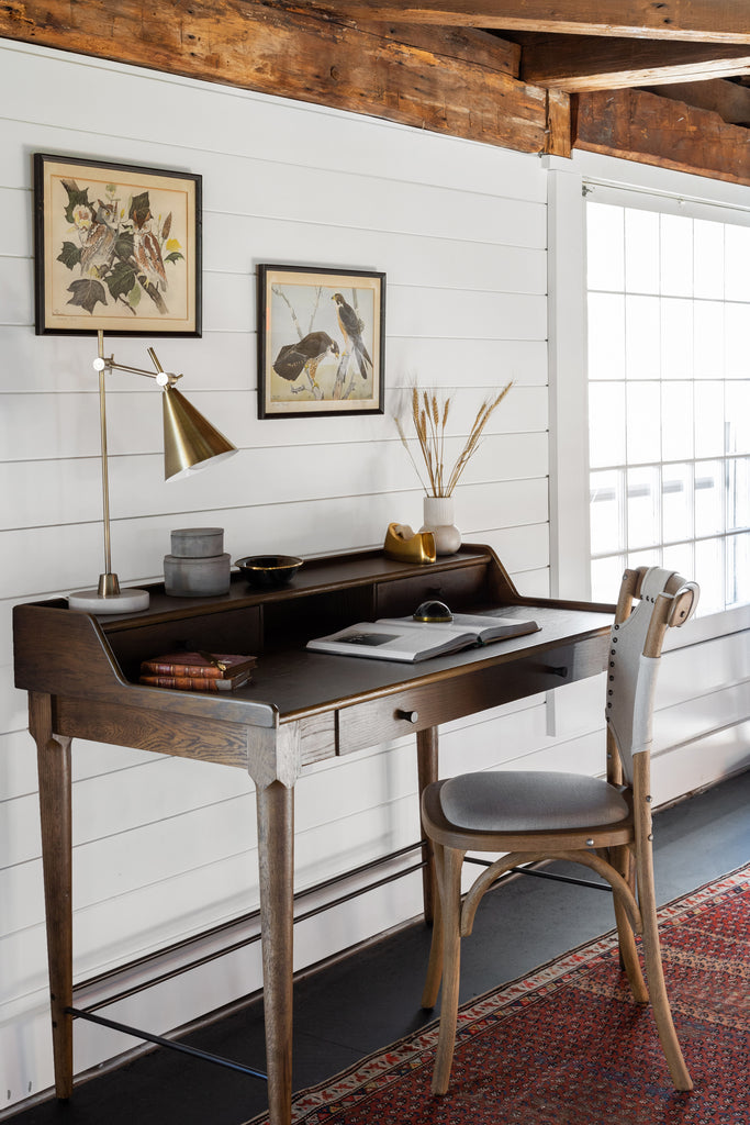 Four Hands Moreau Writing Desk by a window in a room with white walls and wood beams