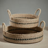 Set of two low round woven basket with black accent and handles on a grey background
