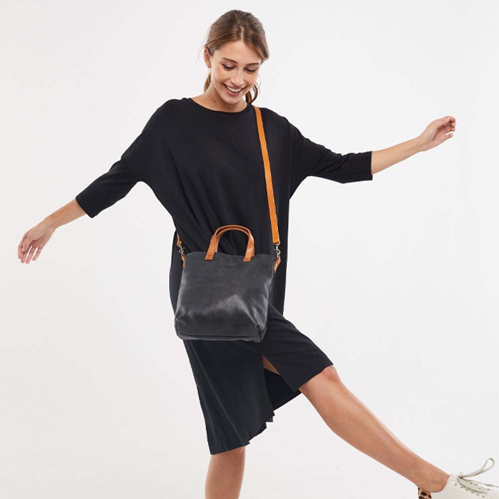 Model wearing Able brand Abera Commuter bag in Black leather with cognac accents on a white background.