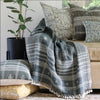 Charcoal grey hand loomed square throw pillow with fringe among other throw pillows on leather sofa