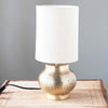 Antique brass finish Metal Table Lamp with etched pattern and Linen Shade on a wood table with grey wall behind